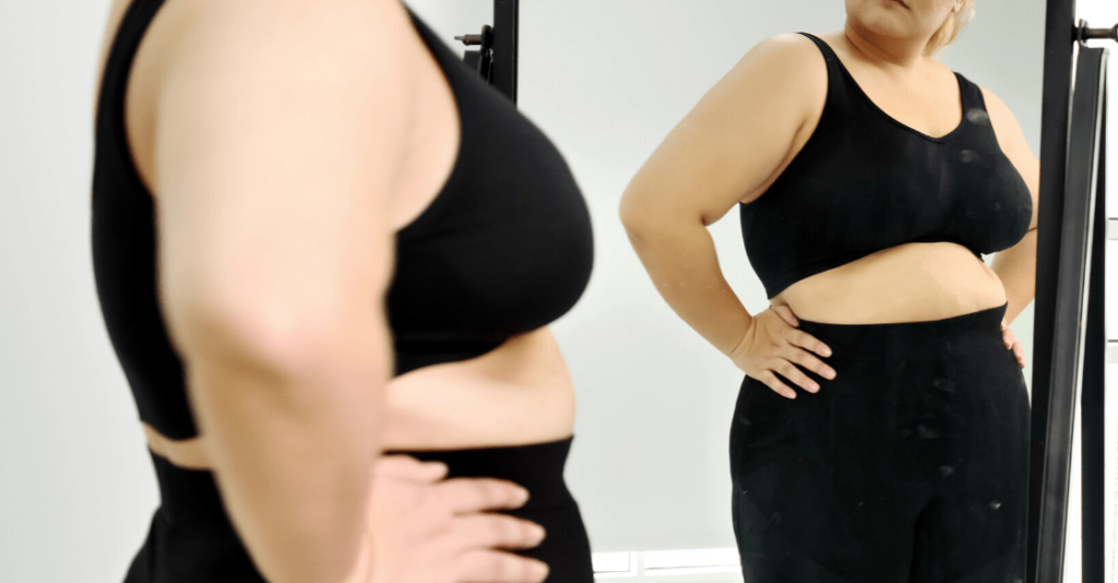 Woman looking in a mirror at her loose skin after weight loss